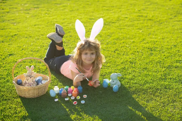 Paashaas kinderen schilderen eieren. Kind jongen in konijn Pasen oren schilderen eieren. — Stockfoto