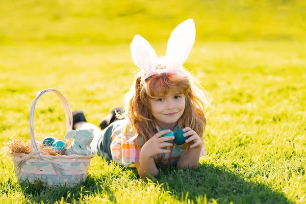 Paashaas kinderen liggen op gras. Kids jongen in konijnenoren jagen op paaseieren in het park buiten. — Stockfoto