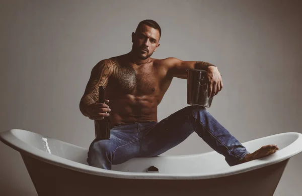 Sexy homme musclé séduisant assis sur la baignoire dans la salle de bain, les hommes vacances avec du champagne. Célébrer Noël ou anniversaire. Partie de sexe privé. — Photo