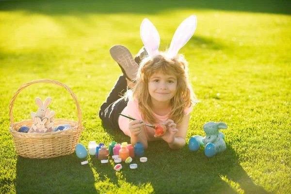 Barnpojke med påskägg och kaninöron som lägger på gräsmålning ägg. — Stockfoto