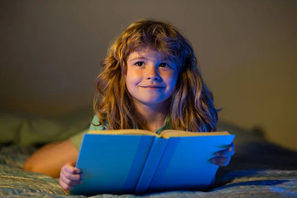 Barnpojkens läsbok. Barn läser en bok i sängen innan de somnar. Barn läser en bok om sänggåendet. Pojke läser godnattsaga, saga. — Stockfoto