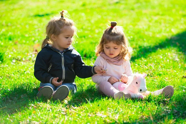 Korsanlık yapan çocuklar. Tatlı oğlan ve kız yaz tarlasında çimenlerde oturuyorlar. Mutlu çocuklar bahar parkında yeşil çimlerde oynuyorlar.. — Stok fotoğraf