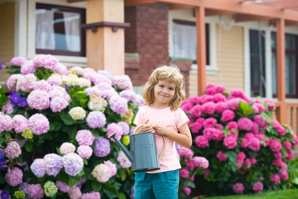 Американський хлопчик на подвір'ї. Сладке дитинство. Щаслива дитина поливає квіти водою в саду.. — стокове фото