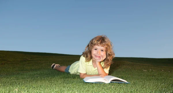 Умный мальчик читает книгу в парке на открытом воздухе. Умные дети. Ребенок в футболке веселится, читая книгу в парке. — стоковое фото