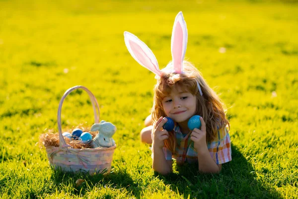 Menino em traje de coelho com orelhas de coelho caçando ovos de Páscoa no parque. — Fotografia de Stock