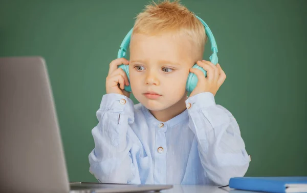 Malý chlapec ve sluchátkách sledovat video lekci na počítači ve škole, dítě ve sluchátkách mají online lekci, pomocí notebooku. Školení počítače. — Stock fotografie