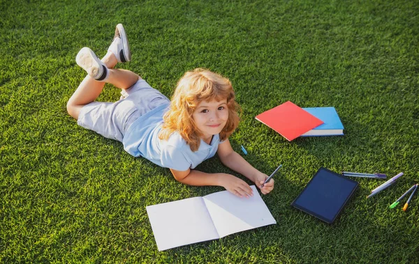 Mignon garçon écriture sur notebook sur herbe verte. — Photo