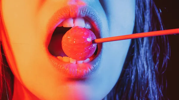 Glamour Mund leckt leckeren Lollypop mit roten Lippen. Lutscht Lolli-Pop. Sexy weibliche Lippe. Sinnliche Frau rote Lippen mit einem Lutscher. Schokoriegel im Neonlicht-Konzept. — Stockfoto