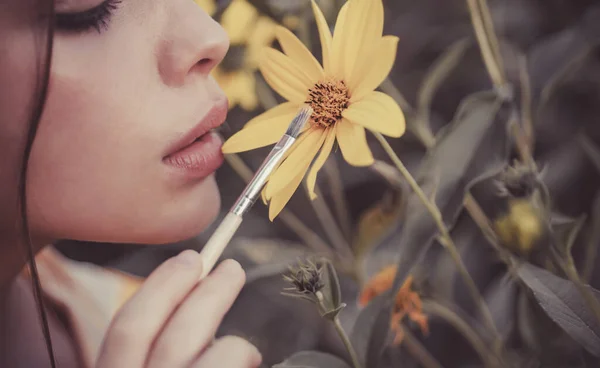 Cara de mulher de verão. Close up retrato de jovem mulher atraente pintando flores amarelas com escova. Flores flor e primavera jardim conceito. Mulher bonita andando no jardim da flor . — Fotografia de Stock