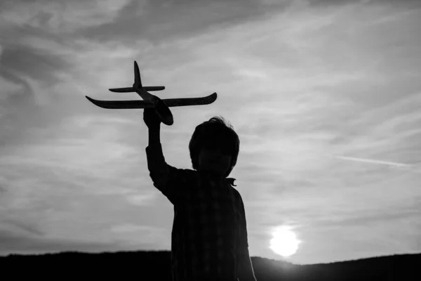 Ragazzino aviatore al tramonto. Bambini piccoli con aeroplano giocattolo in un campo al tramonto. Concetto di successo e leader infantile. — Foto Stock
