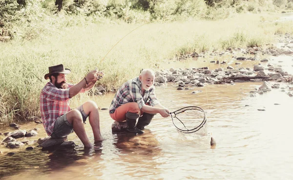 Vader met zoon op de rivier genieten van vissen houden hengels. Gelukkig familieconcept-vader en zoon samen. — Stockfoto