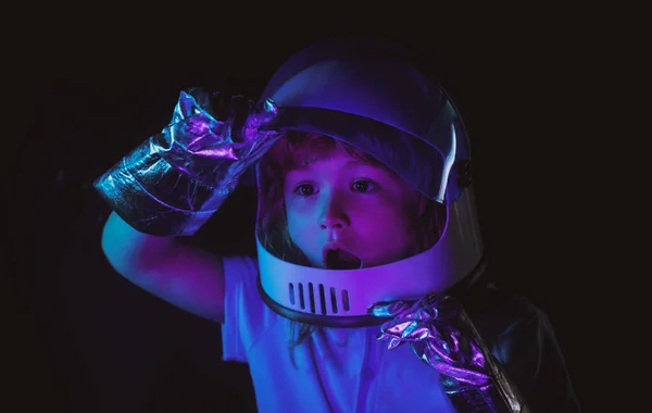 Un niño sueña con convertirse en astronauta y volar al espacio. Cosmos niños en traje espacial y sueños casco. De cerca la cara de los niños emocionados en color neón. — Foto de Stock