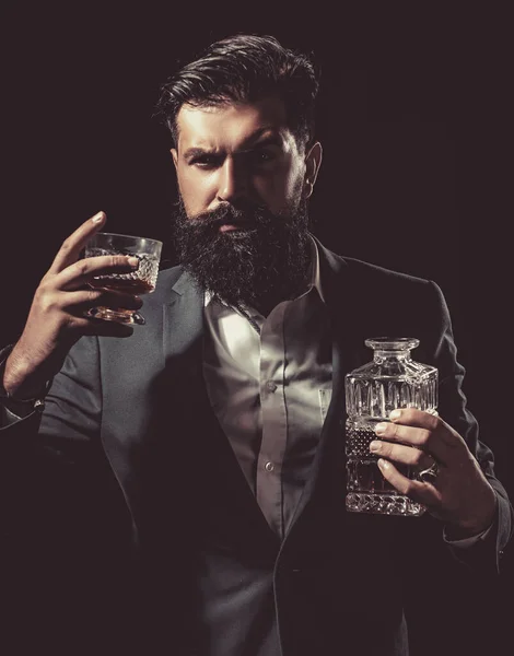 Atrakcyjny barman w barze whisky. Stylowy bogaty człowiek trzyma szklankę starej whisky. Człowiek z brodą trzyma brandy szklaną. — Zdjęcie stockowe