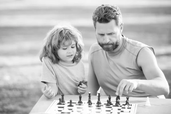 Hijo tendido en la hierba y jugando ajedrez con el padre. Niño concentrado desarrollando estrategia de ajedrez, jugando al juego de mesa con los padres. Juegos y actividades para niños. —  Fotos de Stock