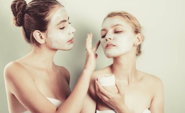 Yüzlerine nemlendirici krem süren iki genç kadın. Kaplıca tedavisi gören dikkatli arkadaşların fotoğrafı. Evde bakım..