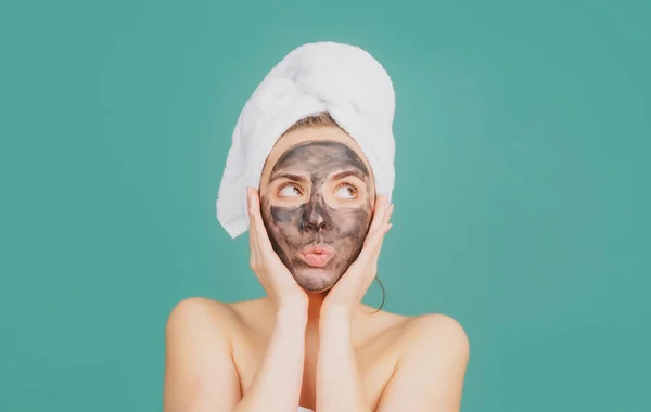 Young beautiful woman in a mask for the face of the therapeutic black clay. Spa treatment. Cosmetic mud facial procedure, spa health concept. Skin care beauty treatment. Towel on head. Medical mud. — Stock Photo, Image