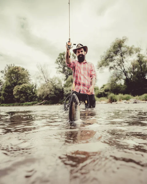 Uomo pesca e relax mentre godendo hobby. Felice pescatore pesca in fiume tenendo canne da pesca. Trota iridea testa d'acciaio. Trota fario pescato nella rete da pesca . — Foto Stock