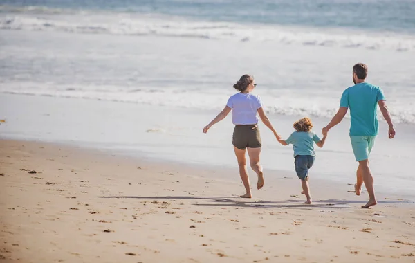 日没時にビーチで走る幸せな家族。家族旅行のコンセプト。健康な人. — ストック写真