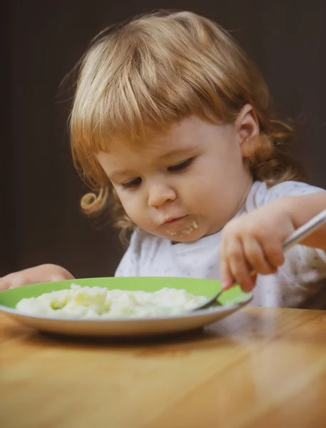 Gyerekevés, táplálkozás. Aranyos baba arc egy kanállal és egy tányér a konyhában otthon. — Stock Fotó