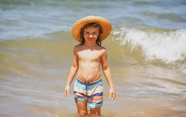 Adorabile bambino in cappello di paglia in spiaggia durante le vacanze estive. Ritratto di bambino giocherellone sullo sfondo del mare. divertente estate bambino faccia. — Foto Stock