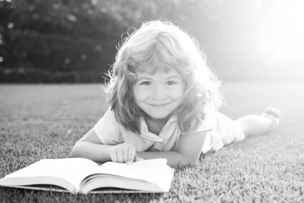 Rapaz a ler o livro de interesses no jardim. Divertimento de verão. Rapaz bonito deitado na grama lendo um livro de crianças. — Fotografia de Stock