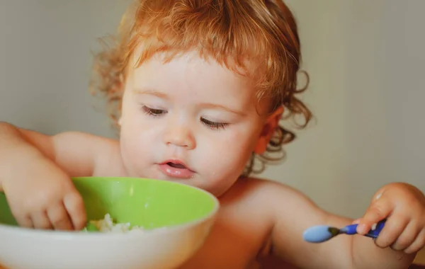 Funny little baby in the kitchen eating with fingers from plate. Healthy nutrition for kids. — Stock Photo, Image