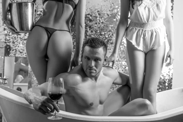 Sexy man in bath drink wine. Threesome concept. Three people in bathtub together. Swinger, orgy or trio in bath. Bisexual lady. Sexual fantasy.