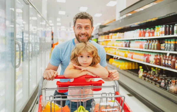 Εκπληκτική οικογένεια πατέρας και παιδί γιος με καλάθι αγορών αγοράζουν τρόφιμα σε παντοπωλείο ή σούπερ μάρκετ. Έκπληκτη φάτσα. Αγοραστής με ψώνια. — Φωτογραφία Αρχείου