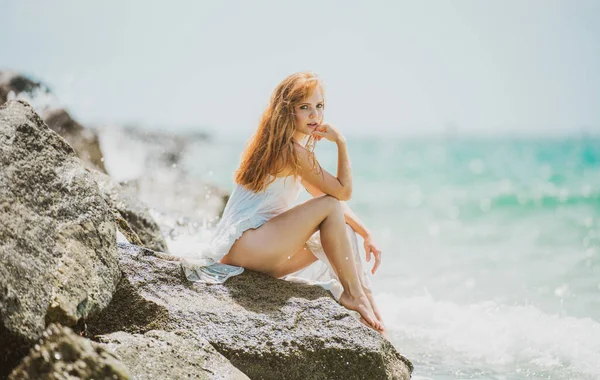 Sinnliche Frau am felsigen Sandstrand vor blauen Wellen. Sommermädchentraum. Attraktive junge Frau im sexy Sommerkleid am Strand. — Stockfoto