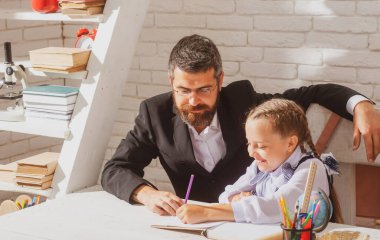 Sınıfta öğretmen olan ilkokul öğrencisi. Öğrenci kız, öğretmeniyle birlikte ders çalışıyor ve yazı yazıyor. Okul malzemeleriyle masasının yanında gülen surat ifadesiyle sevimli kız dersleri alıyor..
