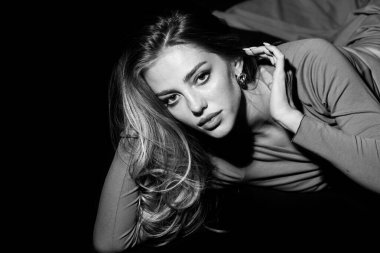 Stüdyoda poz veren genç bir kadın. Siyah stüdyoda şehvetli baştan çıkarıcı pozlar veren seksi bir kız. Yüzünde siyah ışık olan güzel bir kadının moda portresi..