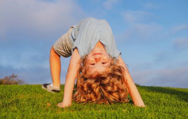 Yeşil çimlerin üzerinde baş aşağı duran mutlu çocuk. Gülen çocuk bahar parkında eğleniyor. Sağlıklı çocuk yaşam tarzı konsepti.