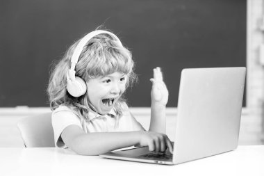 Heyecanlı bir öğrenci, hayrete düşmüş bir öğrenci dizüstü bilgisayara kulaklık takıyor, müzik dersi bilgisayarı kullanıyor. Video çağrısı, öğretmenle uzaktan eğitim..