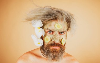 Yüzünde balçık maskesi ve salatalık dilimleri olan komik bir adam. Erkek spa, cilt bakımı, sağlık ve yüz bakımı konsepti.