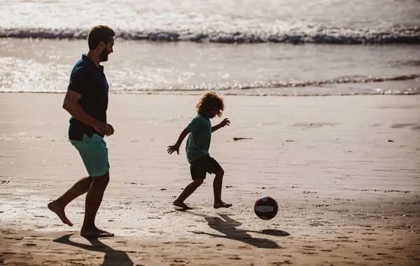 父と子供の屋外で、日没のシルエットを再生します。父と息子は夏休みにビーチでサッカーやサッカーをします。夏の日に遊んでいる子供の男の子とパパ. — ストック写真