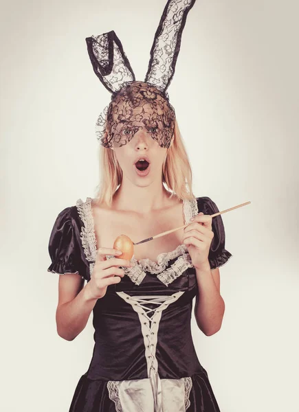 Mujer joven y feliz pintando huevos sobre un fondo blanco. Una joven atractiva con orejas de conejo. Feliz Pascua. Conejo gracioso conejo. Cara de expresión . —  Fotos de Stock