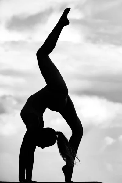 Chica silueta gimnástica en el cielo. Joven chica delgada haciendo acrobacias. Gimnasta en contraluz. —  Fotos de Stock