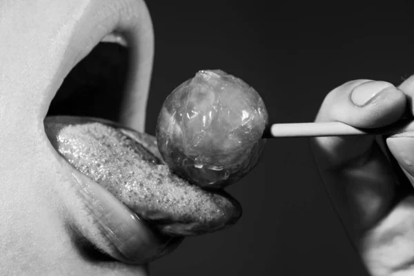 A lamber lábios de língua. Menina com boca sexy comendo chupa chups de perto. Lábios de mulher chupando pirulito. Mulher segurando pirulito na boca, de perto. Lábios vermelhos, conceito sensual e sexy. — Fotografia de Stock