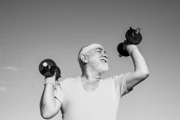 Old mature man exercising with dumbbell. Portrait of senior man holding dumbbell. Old man holding his hands in front of him while lifting dumbbells. — Stock Photo, Image