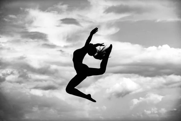 Mujer silueta gimnástica. Mujer gimnasta sobre fondo de cielo azul. Gimnasta silueta haciendo el salto splits. —  Fotos de Stock