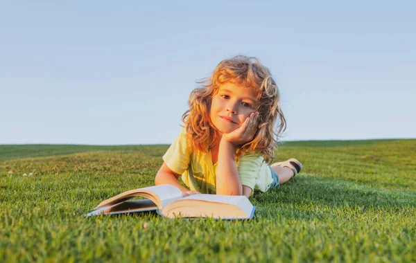 Милый ребенок читает книгу на улице в летнем парке на траве. — стоковое фото