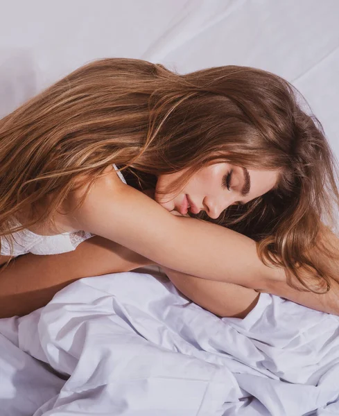 年轻美丽的女孩早上在家里醒来。床上有漂亮脸蛋的性感女人。快乐的女人,卷曲的头发躺在床上,躺在白色的亚麻布上.美梦. — 图库照片