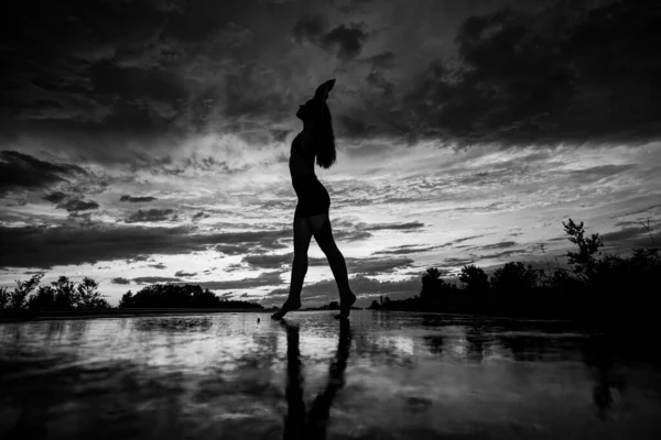 Чорний силует красивої дівчини або красивої жінки, сексуальна струнка модель, з довгим волоссям позує на морському пляжі на заході сонця на жовтому фоні неба — стокове фото