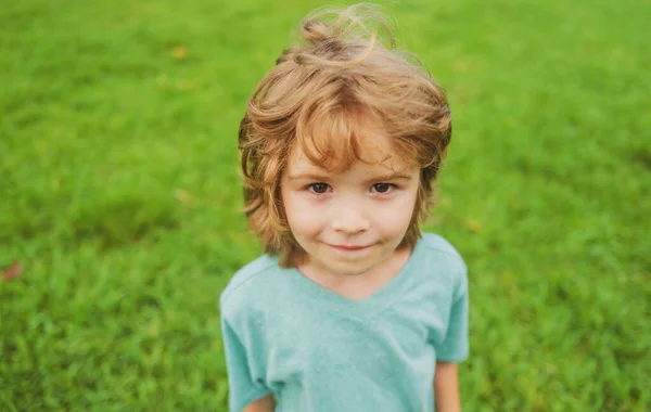 Närbild attraktiv skrattande pojke. Begreppet känslor hos barn. Porträtt av unga leende barn utomhus. Gräs bakgrund. — Stockfoto
