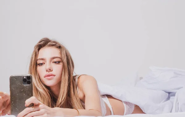 年轻的性感女人在床上用智能手机. — 图库照片