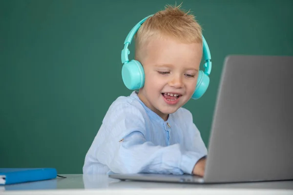 Menino bonito usando fones de ouvido, estudar com laptop em sala de aula, ouvir curso de aula de áudio. Educação, escola, tecnologia e conceito de crianças. — Fotografia de Stock