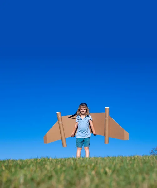 Criança pequena joga astronauta ou piloto. Criança no fundo do céu azul. Crianças com asas de papel sonhos jetpack. As crianças imaginam sonhos de voar. Engraçado garoto com brinquedo jet pack. — Fotografia de Stock