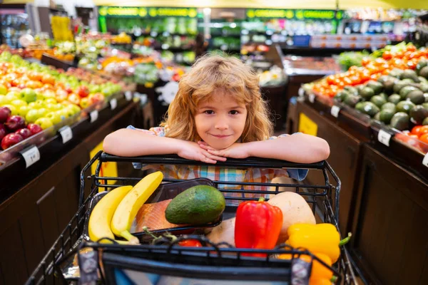 Cibo sano per giovani famiglie con bambini. Ritratto di bambino sorridente con carrello pieno di verdure fresche. Cibo sano per bambini. Bambino nel supermercato compra verdure. — Foto Stock