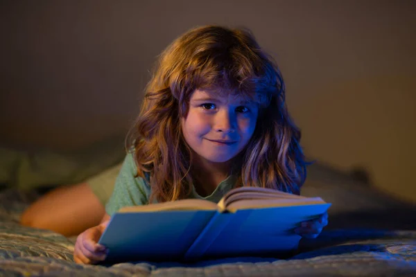 Criança lendo um livro na casa escura. Rapaz feliz sentado na sala de estar a ver fotografias no livro de histórias. O miúdo a fazer trabalhos de casa para a escola primária. Estudo de crianças. — Fotografia de Stock