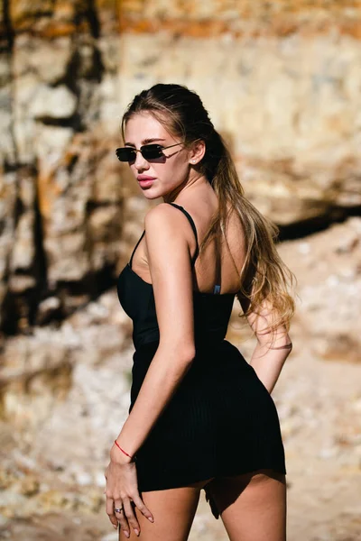 Fashion vrouw in trendy zonnebril en mode zwarte jurk buiten. Fashion vrouw in de zomer, sexy pose. — Stockfoto